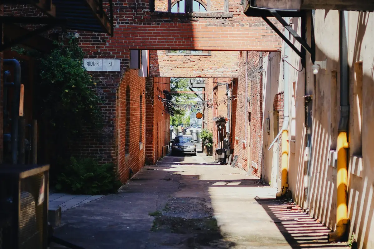 A narrow brick alley between older commercial buildings, with downspouts along the wall