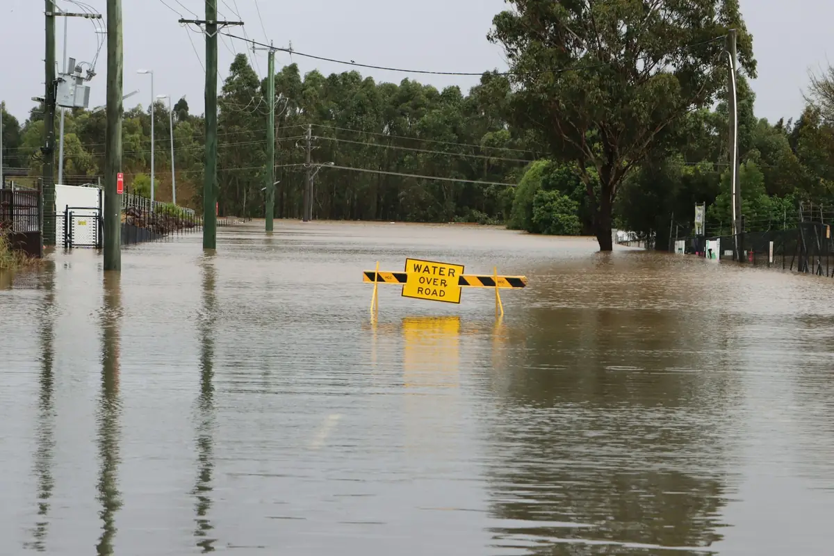 A flooded road with a yellow water over road sign standing in brown water