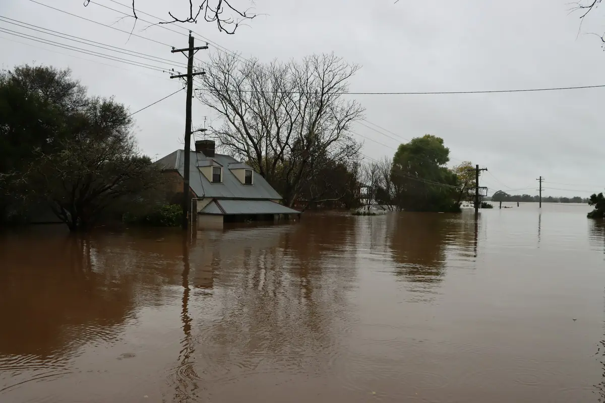 Brown floodwater surrounding a small house and trees under a gray sky